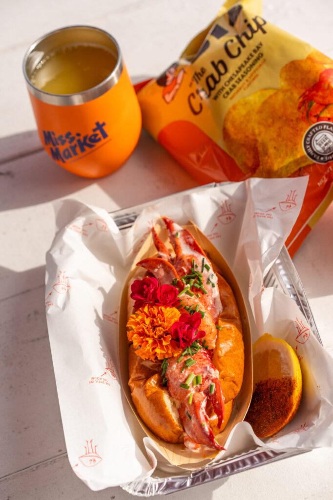 Lobster roll from The Nell Shell topped with marigolds, with crab chips and a Miss Market tumbler