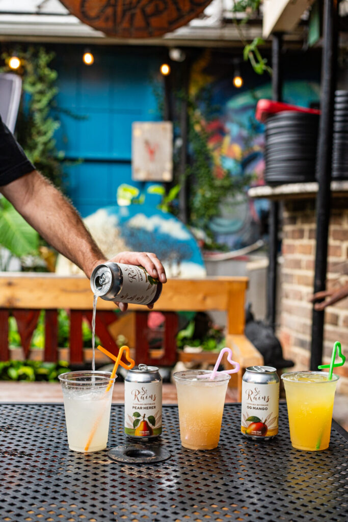 Cans of St. Rains Pear Herer and OG Mango with cocktails on a patio table at MRB Bar & Kitchen