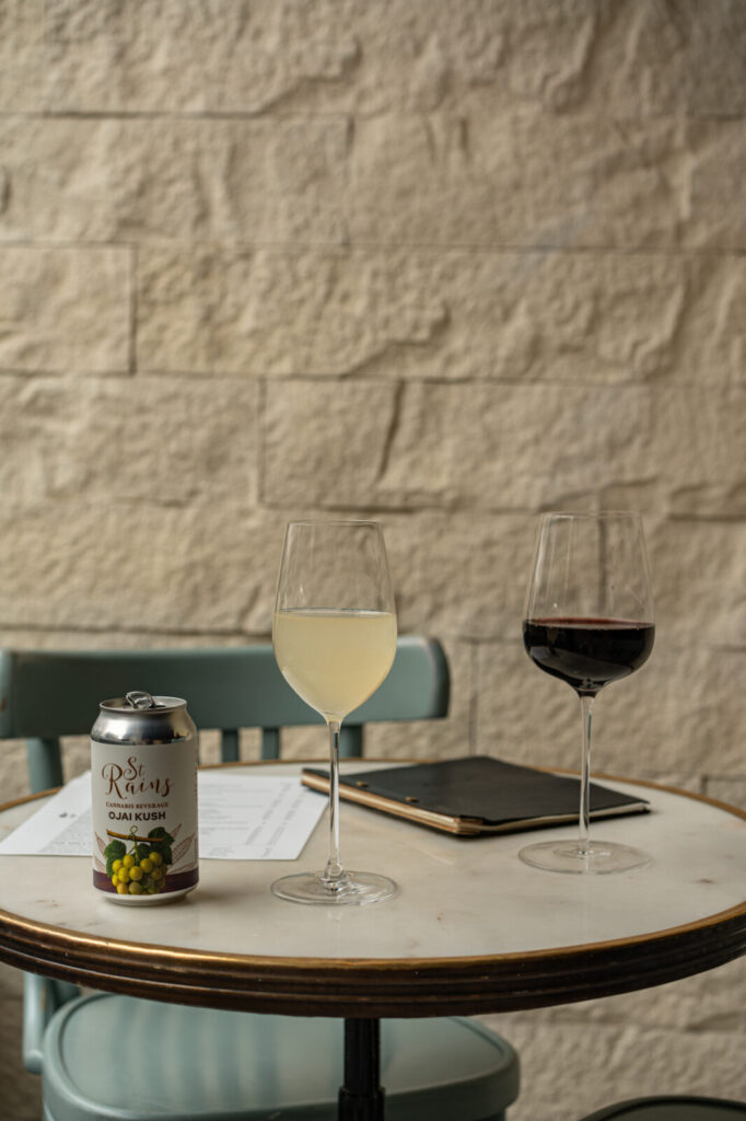 Can of St. Rains Ojai Kush with glasses of white and red wine on a marble table at Pluck Wine Bar
