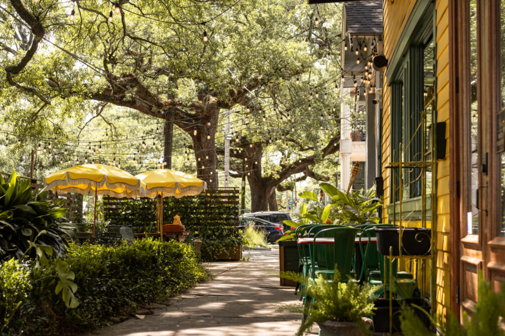 Sidewalk patio at Smoke & Honey in Mid-City with yellow umbrellas and string lights under oak trees