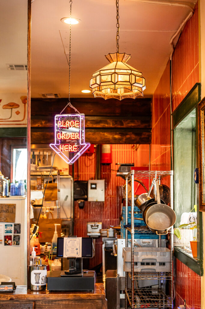 Order counter at Smoke & Honey with a neon Place Order Here sign and stained glass pendant light