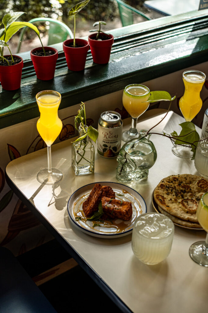 Table at Smoke & Honey with a can of St. Rains Pear Herer, cocktails, saganaki, and flatbread
