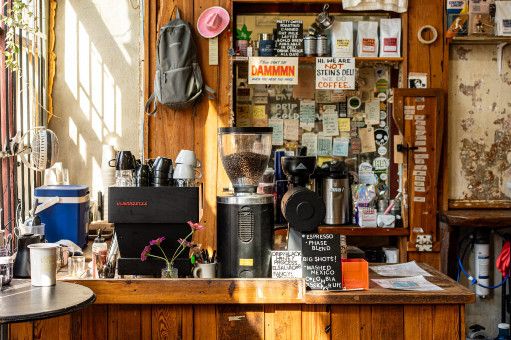 Espresso bar at the front of Stein's Deli with a La Marzocco machine, coffee bags, and handwritten menu boards